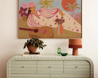 May include: A rectangular wooden dresser with a light green and white striped pattern, featuring seven drawers with small knobs. Above it hangs a framed painting of a person in a pink hat, a guitar, and a vase of flowers under a sun.