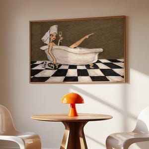 May include: A framed wall art print depicting a person with a white towel wrapped around their head, relaxing in a white clawfoot bathtub. The person holds a glass of champagne and a magazine. The floor features a black and white checkered pattern.