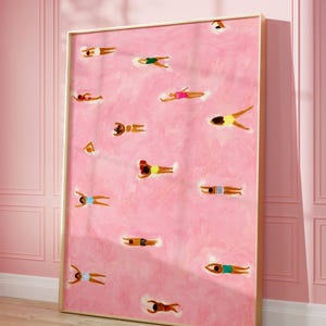 Puede incluir: Una impresión artística enmarcada que presenta un fondo rosa con múltiples figuras flotando en el agua. Las figuras visten trajes de baño de varios colores, incluyendo amarillo, rosa y azul. La obra de arte se exhibe en un marco dorado.