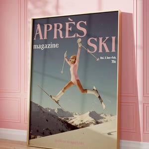 Pode incluir: Pôster vintage emoldurado com as palavras "APRÈS SKI" e "magazine". A imagem apresenta uma pessoa com um traje de esqui rosa saltando sobre esquis, com um fundo de montanhas nevadas. O pôster está em uma moldura dourada.