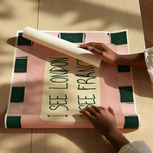 Puede incluir: Un p&oacute;ster rectangular con fondo rosa claro y un borde a cuadros verde oscuro. El centro contiene un rect&aacute;ngulo de color crema con el texto en verde oscuro I SEE LONDON I SEE FRANCE escrito en una fuente de estilo manuscrito.