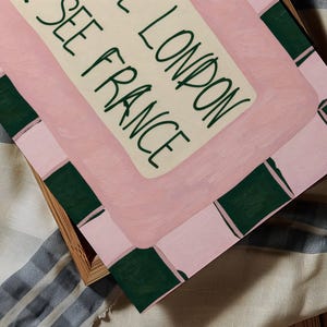 Puede incluir: Una impresi&oacute;n art&iacute;stica rectangular con un fondo rosa claro y acentos rectangulares de color verde oscuro en los bordes. El centro contiene un panel color crema con el texto verde oscuro "SEE LONDON SEE FRANCE" en estilo manuscrito.