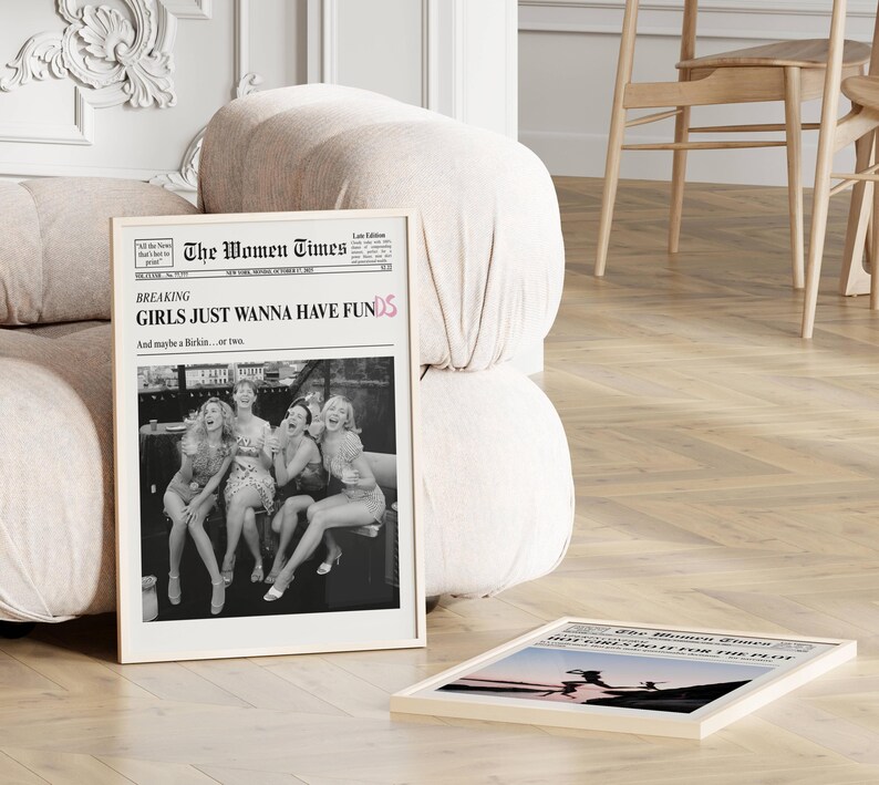 Op de afbeelding: Een ingelijste verticale poster getiteld The Women Times met een zwart-witfoto van vier lachende mensen. De kop luidt Breaking Girls Just Wanna Have Funds en And maybe a Birkin... or two. Een tweede ingelijste poster ligt op de grond.