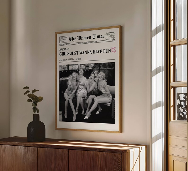 Op de afbeelding: Een ingelijste wandposter met een krantenopmaak getiteld The Women Times. De kop luidt BREAKING GIRLS JUST WANNA HAVE FUNDS met de subkop And maybe a Birkin... or two. Daaronder staat een zwart-witfoto van vier personen afgebeeld.