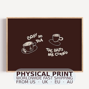 Könnte beinhalten: Ein dunkelbrauner, rechteckiger Wandkunstdruck in einem hellen Holzrahmen mit weißen Strichzeichnungen von zwei Teetassen auf Untertassen. Der Text lautet "BODY SO TEA" und "THE BRITS ARE COMING" in einem lockeren, handgezeichneten Stil.