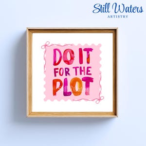 May include: A framed print with the words "DO IT FOR THE PLOT" in watercolor lettering. The text is in shades of red, orange, and purple on a pink postage stamp design. The frame is made of light-colored wood.