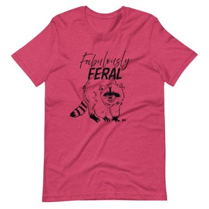 May include: A pink t-shirt with a black illustration of a raccoon and the text "Fabulously Feral".