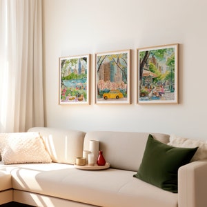 May include: Three framed watercolor paintings depicting scenes from New York City. The first painting shows a view of the city skyline from Central Park, with people picnicking in the foreground. The second painting shows a yellow taxi cab driving through Central Park, with cherry blossoms in bloom. The third painting shows a street scene in New York City, with people sitting at outdoor tables.
