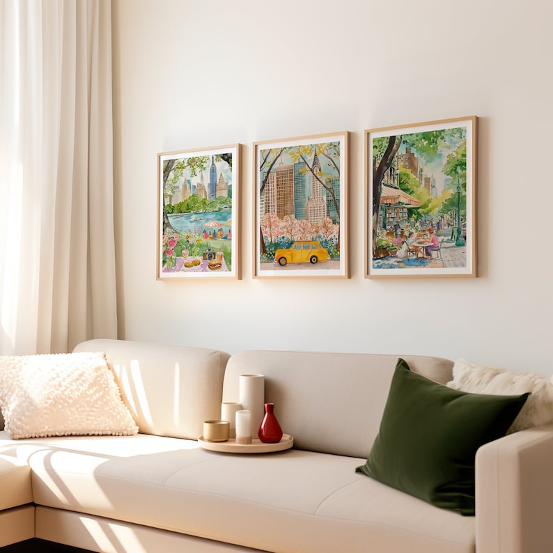 May include: Three framed watercolor paintings depicting scenes from New York City. The first painting shows a view of the city skyline from Central Park, with people picnicking in the foreground. The second painting shows a yellow taxi cab driving through Central Park, with cherry blossoms in bloom. The third painting shows a street scene in New York City, with people sitting at outdoor tables.