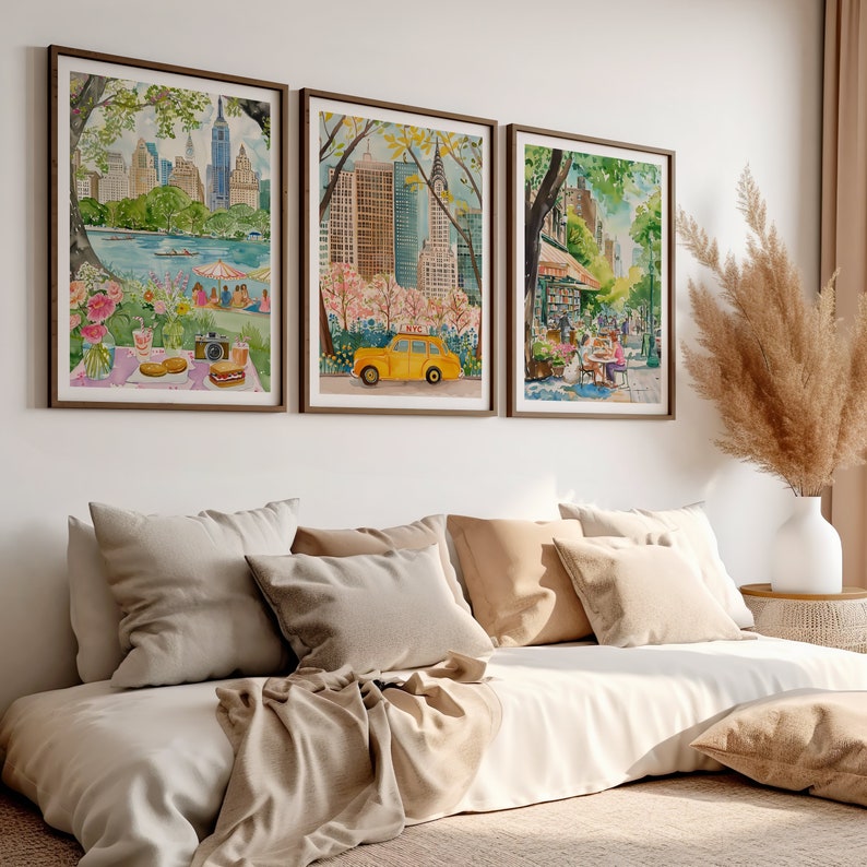 May include: Three watercolor paintings of New York City scenes. The first painting shows a park with a picnic blanket and a yellow taxi cab. The second painting shows a cityscape with a yellow taxi cab. The third painting shows a street scene with people sitting at a cafe.