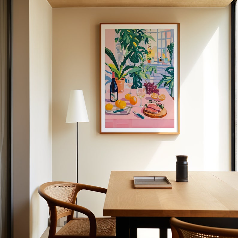 Puede incluir: Una impresi&oacute;n enmarcada de un bodeg&oacute;n con un mantel rosa, una botella de vino, una copa de vino, uvas, limones y un plato de carne cortada. La impresi&oacute;n est&aacute; colgada en una pared de un comedor con una mesa y sillas de madera.