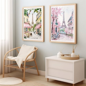 May include: Two framed watercolor paintings of Parisian street scenes with the Eiffel Tower in the background. The painting on the left shows a cafe with pink awnings and the painting on the right shows a street with a bicycle.
