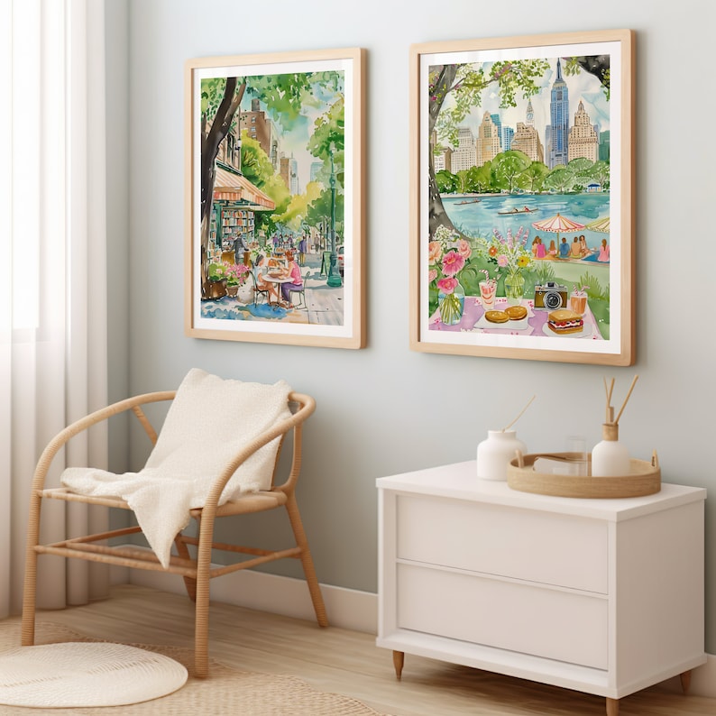 May include: Two framed watercolor paintings depicting scenes in New York City. The first painting shows a street scene with a cafe and people sitting outside. The second painting shows a view of Central Park with a picnic scene in the foreground.