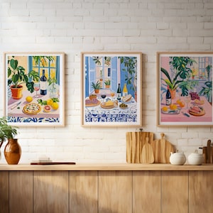 Puede incluir: Tres ilustraciones enmarcadas de escenas de bodeg&oacute;n con comida, vino y plantas. Cada ilustraci&oacute;n presenta una paleta de colores diferente: rosa, azul y amarillo. Las ilustraciones est&aacute;n colgadas en una pared de ladrillo blanco.