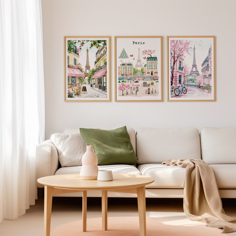 May include: Three framed watercolor paintings depicting scenes from Paris, France. The paintings feature the Eiffel Tower, Parisian streets, and blooming trees. The paintings are hung on a white wall above a white couch.