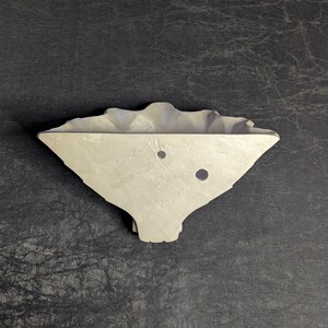 May include: A light gray, asymmetrical, wall-mounted planter with a textured surface. The planter has a wavy top edge and two circular holes. The design is modern and minimalist, suitable for small plants or succulents.