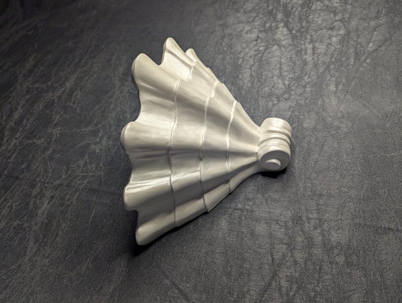 May include: A white, decorative architectural element with a fan-like design. The piece has a series of curved ridges and a cylindrical base with a circular detail. The object is set against a dark, textured background.