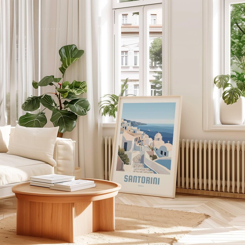 May include: A framed print of a colorful illustration of Santorini, Greece. The print features a white building with blue accents and a winding path leading to the ocean. The text "SANTORINI" is printed in blue at the bottom of the print.