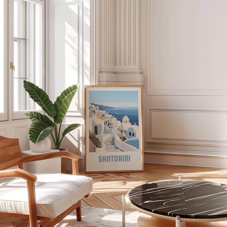 May include: A framed print of a colorful illustration of Santorini, Greece. The print features white buildings with blue accents, a winding street, and a view of the ocean. The text "SANTORINI" is printed at the bottom of the print.
