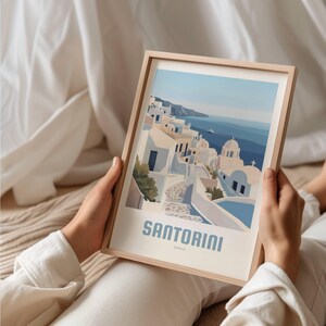 May include: A framed illustration of a cityscape with white buildings and a blue sea. The text "Santorini, Greece" is at the bottom of the image.