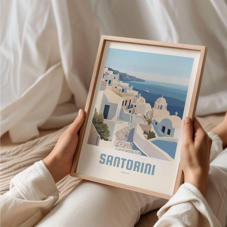 May include: A framed illustration of a cityscape with white buildings and a blue sea. The text "Santorini, Greece" is at the bottom of the image.