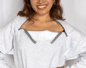 May include: A woman wearing a gray sweatshirt with a zipper that goes down the front. The sweatshirt has a white lining. She is smiling and wearing clear glasses.