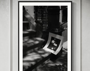 May include: A black and white photograph of a set of stairs with a shadow cast on them. A framed photograph of a street lamp is lying on the stairs.