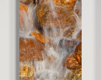 May include: Close-up of a cascading waterfall flowing over smooth, orange-brown rocks. The water is blurred, creating a sense of motion and energy.