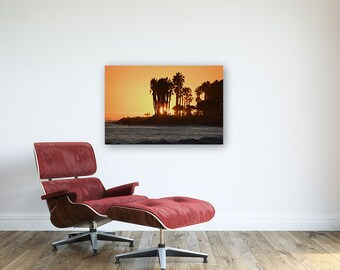 May include: Silhouette of palm trees against a vibrant orange sunset over the ocean. The sky is a gradient of orange, yellow, and pink.