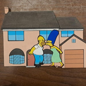 May include: A yellow cartoon character with blue jeans and a white shirt kisses a blue-haired cartoon character wearing a green dress in front of a pink house with a brown roof.