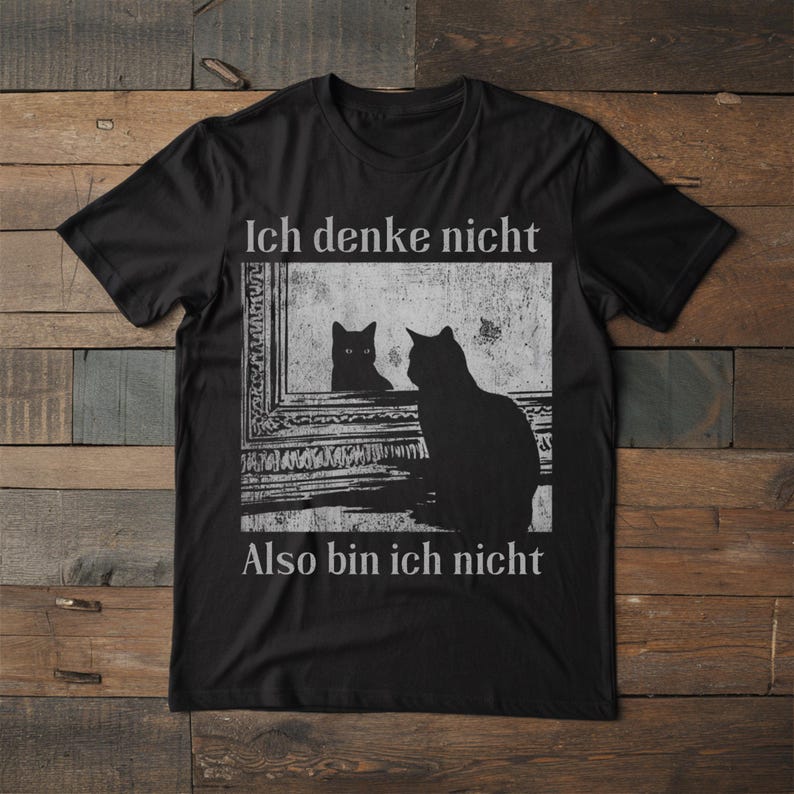 May include: Black t-shirt with a graphic of a cat looking in a mirror at its reflection. The mirror image is also a cat. The text on the shirt reads "Ich denke nicht, Also bin ich nicht."