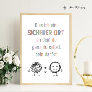 May include: A framed print with the text "Dies ist ein SICHERER ORT an dem du ganz du selbst sein darfst" in pastel colors. Below the text are two cartoon figures holding hands, one a tangled scribble, the other smiling. The print is in a light wood frame.