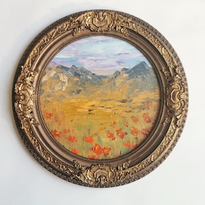 May include: An oval oil painting depicting a landscape with mountains, a field of orange flowers, and a sky with blue and purple tones. The artwork is framed in an ornate, gold-coloured frame.