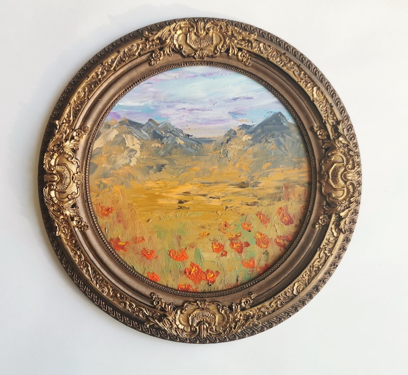 May include: An oval oil painting depicting a landscape with mountains, a field of orange flowers, and a sky with blue and purple tones. The artwork is framed in an ornate, gold-coloured frame.