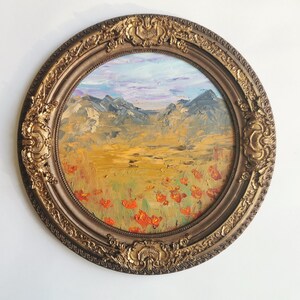 May include: An oval oil painting of a landscape with mountains, a field of red flowers, and a blue and purple sky. The painting is set in an ornate, gold-coloured frame.