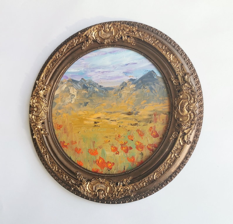 May include: An oval oil painting depicting a mountain landscape with orange flowers in a decorative, gold-toned frame. The sky features blue and purple tones. The painting is created in an impressionistic style.
