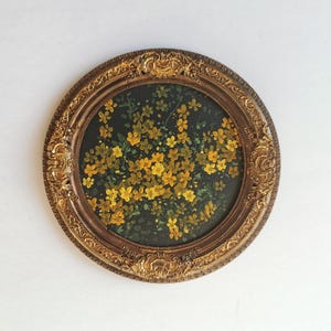 Könnte beinhalten: Ein ovales Gemälde mit gelben Blumen vor einem dunkelgrünen Hintergrund, umrahmt von einem verzierten, antik anmutenden, goldfarbenen Rahmen, das einen Vintage-Look erzeugt.