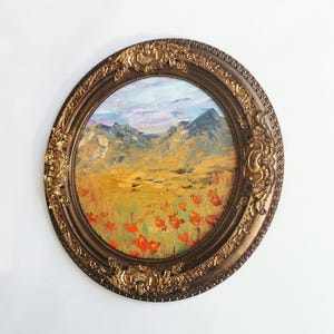 May include: Oval oil painting in a decorative gold frame. The artwork depicts a landscape with mountains, a field of red poppies, and a blue sky with clouds. The frame has ornate detailing.