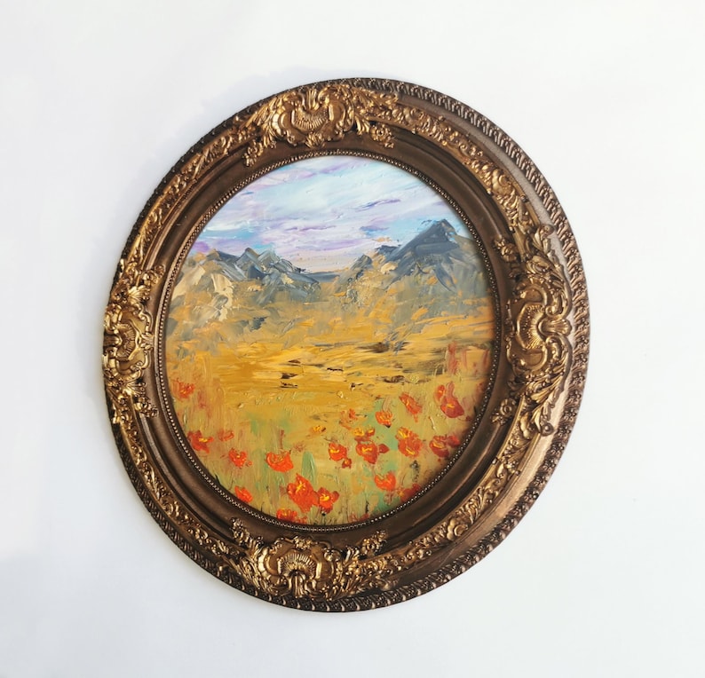 May include: Oval oil painting in a decorative gold frame. The artwork depicts a landscape with mountains, a field of red poppies, and a blue sky with clouds. The frame has ornate detailing.
