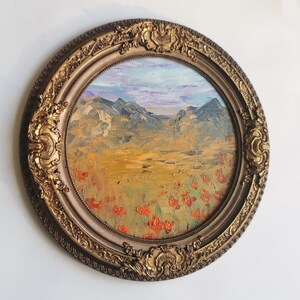 May include: An oval oil painting of a mountain landscape in a gold ornate frame. The painting shows a field of red flowers, a golden meadow, and mountains under a blue and purple sky. The frame features detailed scrollwork.