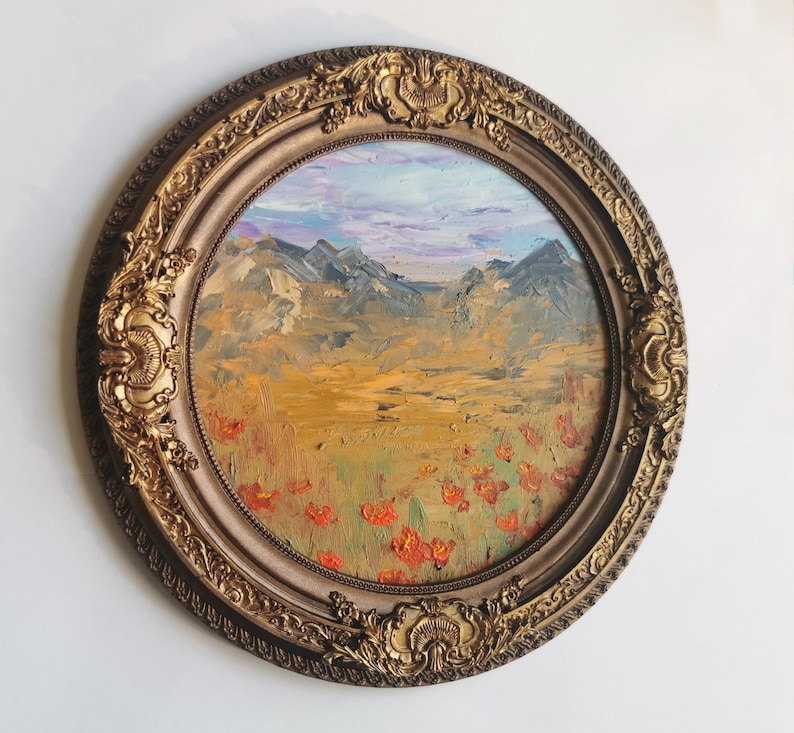 May include: An oval oil painting of a mountain landscape in a gold ornate frame. The painting shows a field of red flowers, a golden meadow, and mountains under a blue and purple sky. The frame features detailed scrollwork.