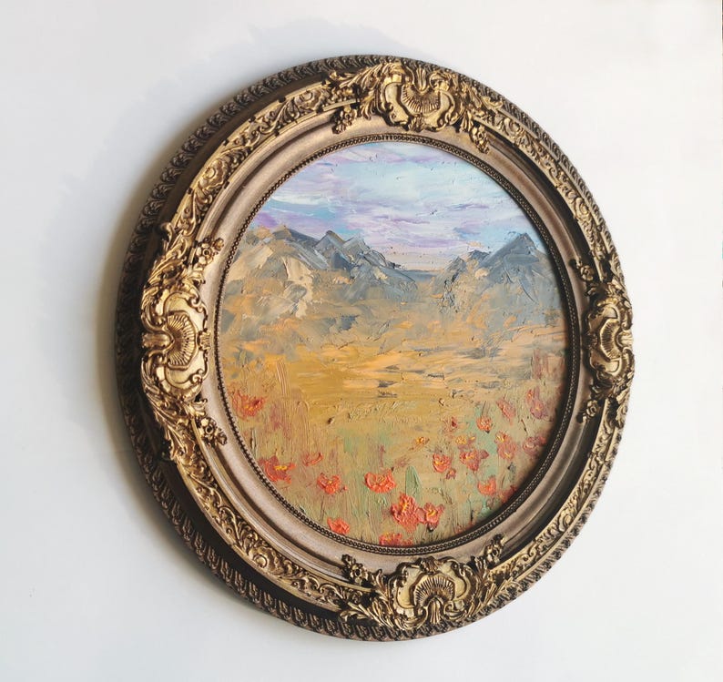 May include: A circular oil painting in a gold ornate frame. The landscape shows mountains, a field of red flowers, and a blue and purple sky. The frame has detailed carvings and a cream-coloured inner border.
