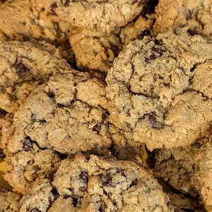 May include: A close-up of a plate of freshly baked chocolate chip oatmeal cookies. The cookies are golden brown and have a chewy texture. They are covered in chocolate chips and oatmeal.