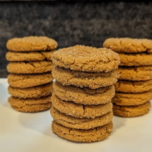 May include: Three stacks of brown gingerbread cookies on a white plate. The cookies are round and have a slightly rough texture.