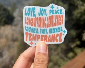 May include: A white sticker with the words "LOVE, JOY, PEACE, LONGSUFFERING, GENTLENESS, GOODNESS, FAITH, MEEKNESS, TEMPERANCE" in blue and orange lettering. The sticker has a sparkly design.