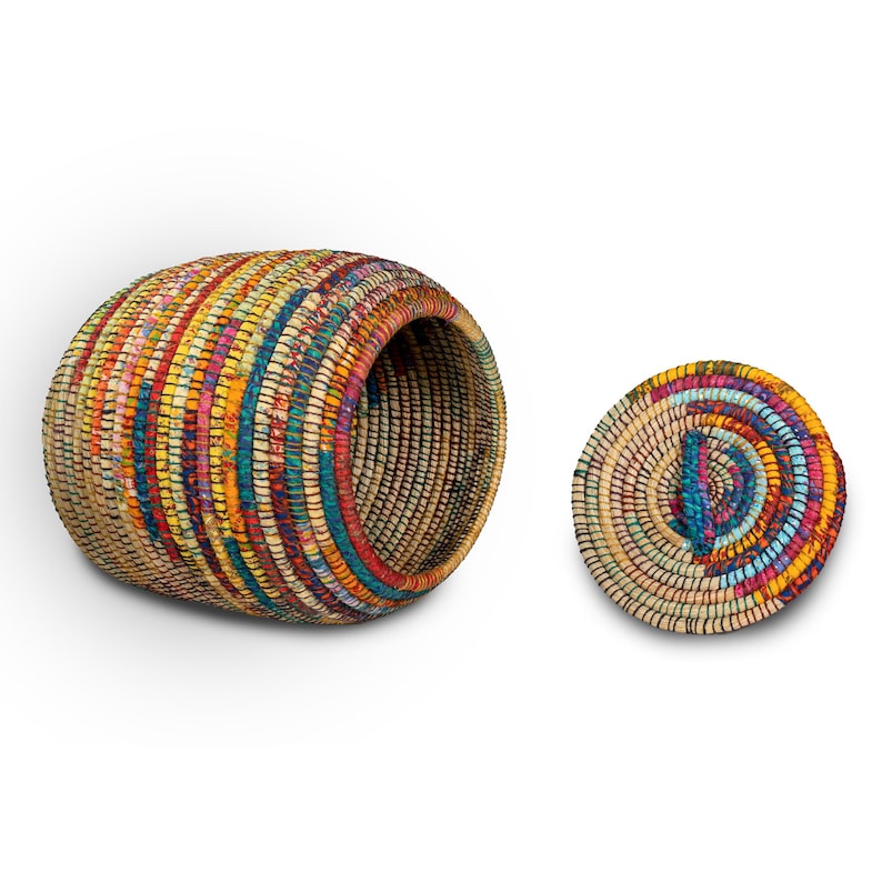 Puede incluir: Una cesta cil&iacute;ndrica hecha a mano con su tapa. La cesta est&aacute; tejida con fibras naturales y tiras de tela coloridas en tonos de rojo, amarillo, azul y verde. La tapa es redonda y plana, con un dise&ntilde;o en espiral.