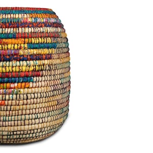 Puede incluir: Una cesta redonda tejida con un dise&ntilde;o colorido y estampado. La cesta presenta una mezcla de colores vibrantes, incluyendo rojo, amarillo, azul y verde, creando una textura visualmente atractiva. La base de la cesta es de color beige natural.