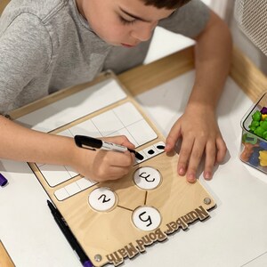 Pu&ograve; includere: Un tabellone di matematica di legame numerico in legno con una superficie bianca cancellabile a secco. Il tabellone ha tre cerchi con i numeri 2, 3 e 5 scritti al loro interno. Il tabellone ha anche una sezione per scrivere numeri e una sezione per disegnare punti. Il tabellone &egrave; etichettato come "Matematica di legame numerico".