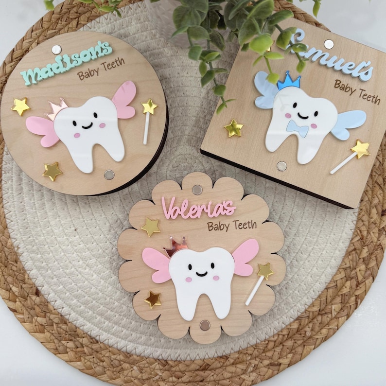 May include: Three wooden tooth fairy boxes with a tooth design and a crown. The boxes are decorated with stars and wings. The names Madison's, Samuel's, and Volerias are written on the boxes.