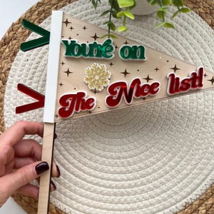 May include: A wooden Christmas sign with the text "You're on the Nice list!" in red, green, and white letters. The sign is decorated with a gold snowflake and stars.